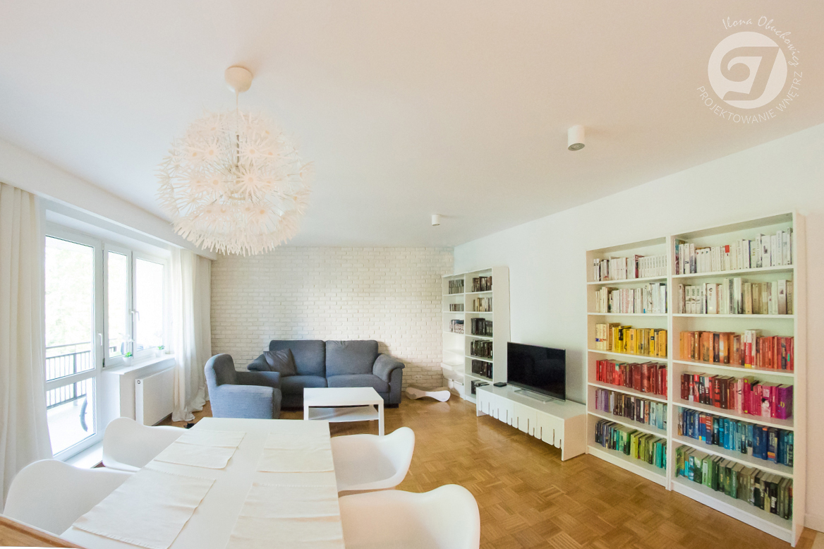 salon w mieszkaniu dwupokojowym z aneksem jadalnym, biblioteka w domu, regały do przechowywania książek, biała cegła na ścianie w salonie, drewniana klepka w salonie